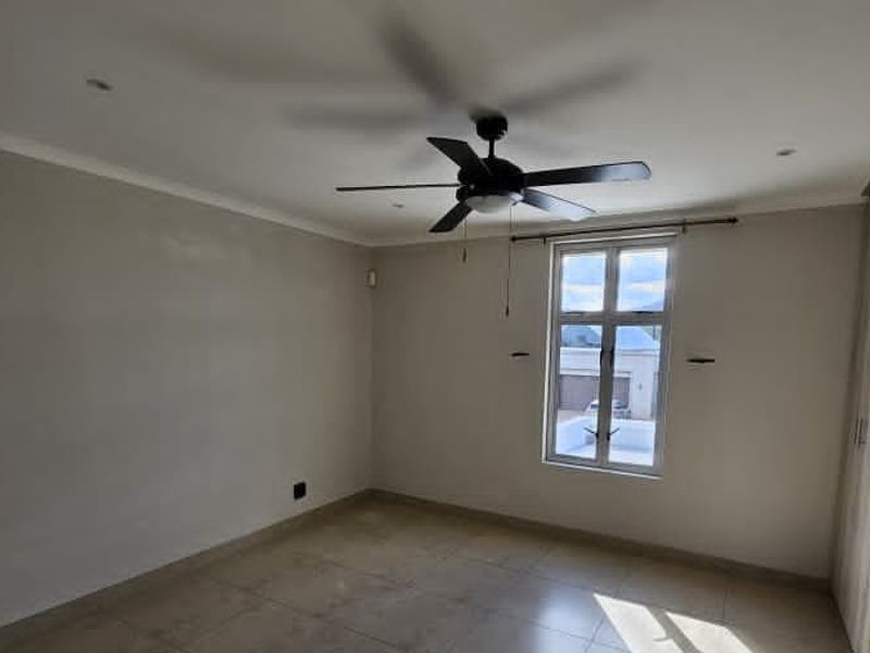 A bright, empty bedroom featuring tiled flooring, a ceiling fan, and built-in cupboards, offering a clean and neutral space ready for personalization.