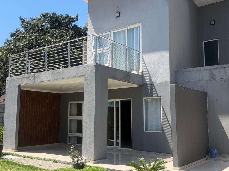 Rear view of a two-story cluster home featuring a covered patio, an upper-level balcony with stainless steel railings, and modern grey exterior finishes.