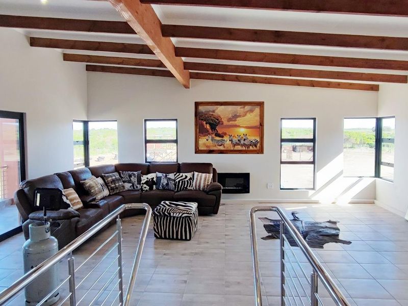Spacious living area featuring exposed timber ceiling beams, tiled flooring, a built-in fireplace, and large windows providing ample natural light and scenic views.