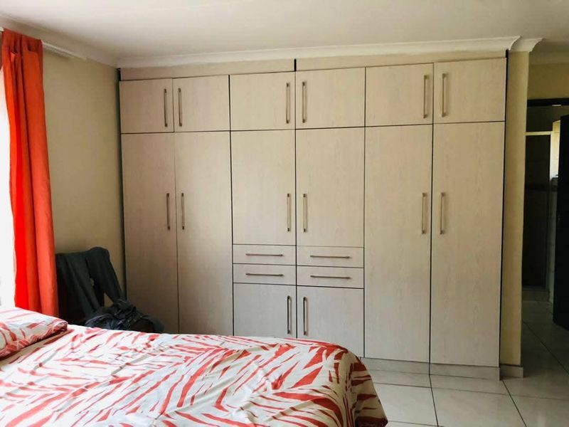 A bedroom featuring extensive floor-to-ceiling built-in cupboards with light wood-grain finish and neutral tiled flooring.