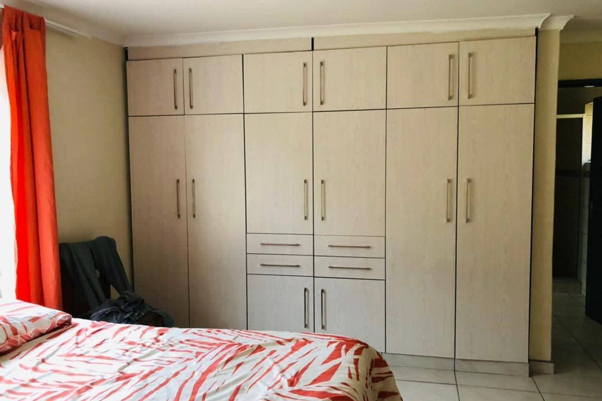 A bedroom featuring extensive floor-to-ceiling built-in cupboards with light wood-grain finish and neutral tiled flooring.