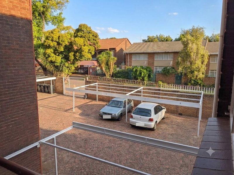 An elevated view of the apartment complex rear parking area featuring paved surfaces and covered carport structures.