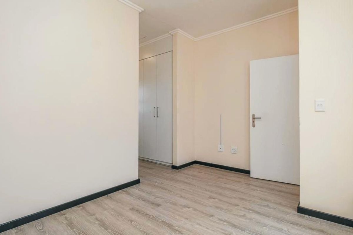 A bright, empty bedroom featuring light wood-look laminate flooring, built-in cupboards, and neutral wall finishes.