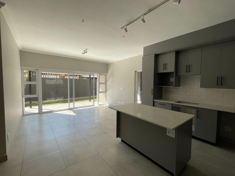Modern open-plan living area featuring a sleek kitchen with island, subway tile backsplash, and large sliding glass doors leading to the outdoor space.