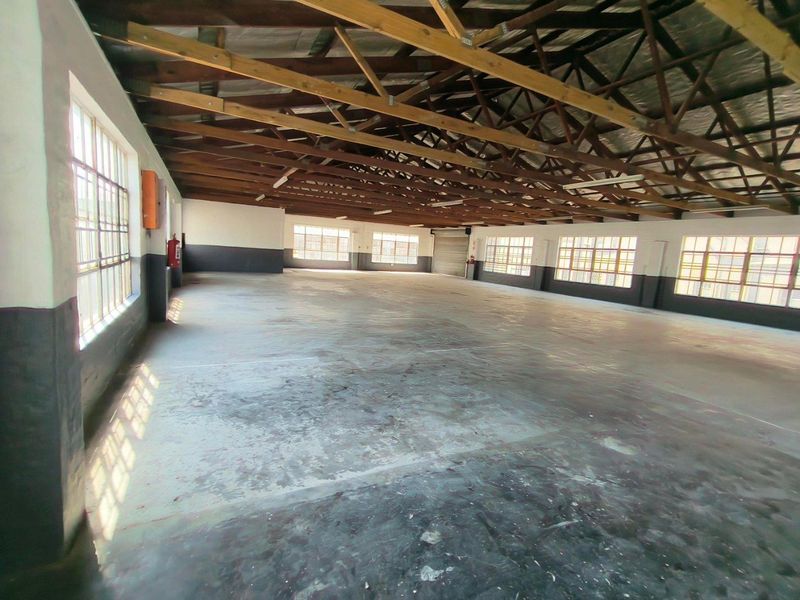 Spacious industrial utility space featuring exposed timber roof trusses, concrete flooring, and large steel-framed windows providing ample natural light.
