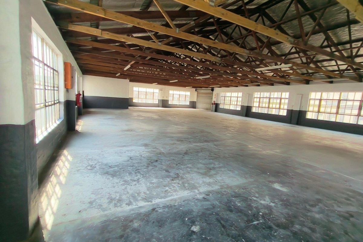 Spacious industrial utility space featuring exposed timber roof trusses, concrete flooring, and large steel-framed windows providing ample natural light.
