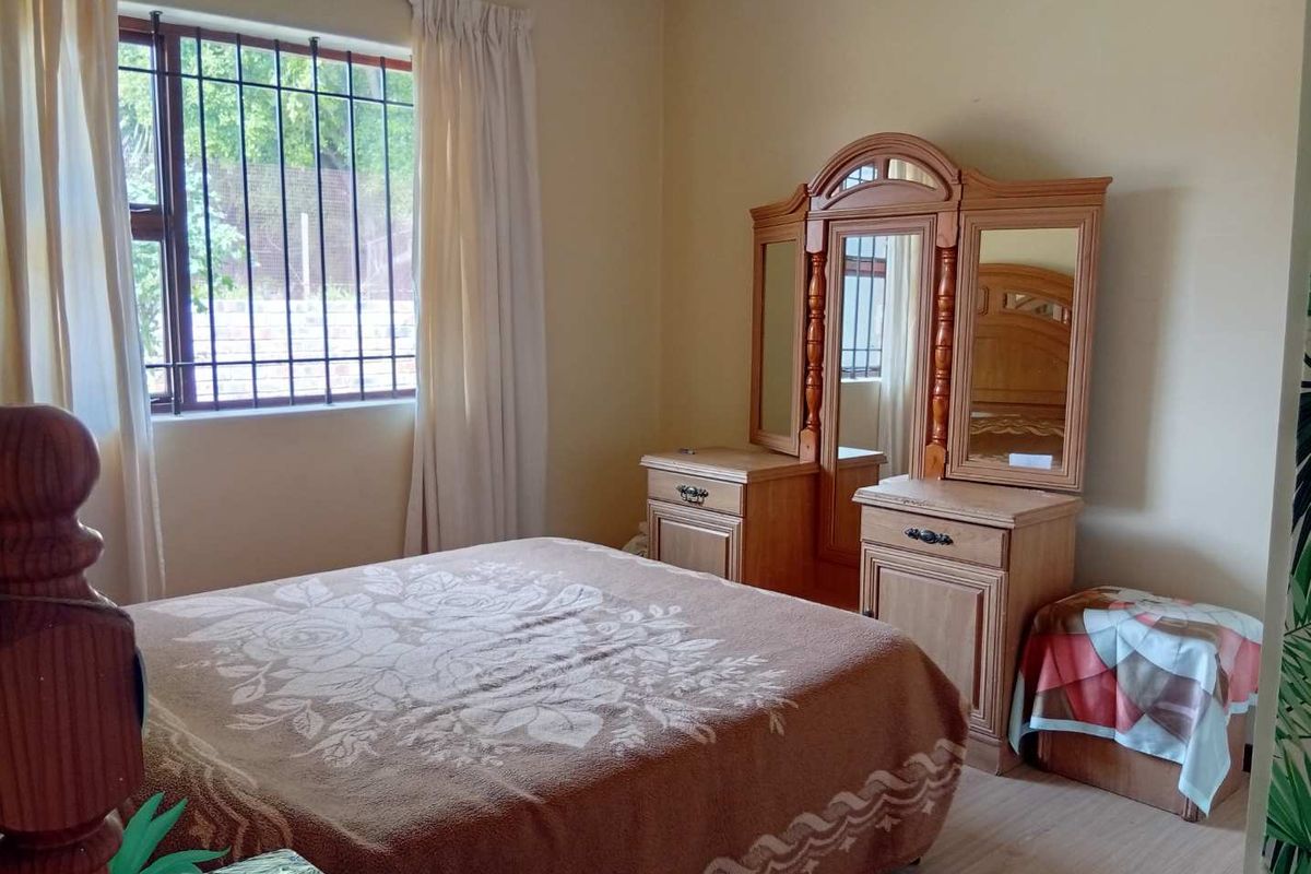 A functional bedroom featuring laminate flooring, neutral wall finishes, and security bars on the window.