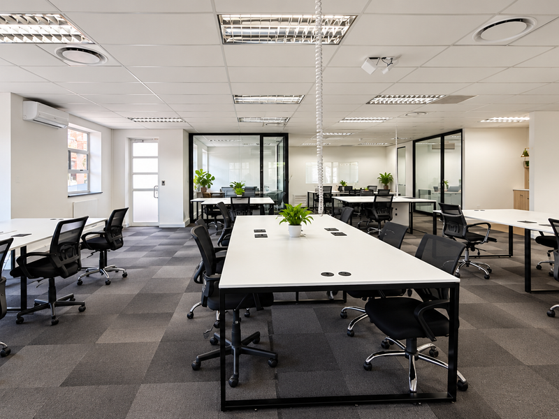 Modern open-plan office space featuring suspended ceilings, recessed lighting, glass partitions, and carpeted flooring, providing a professional and well-lit work environment.