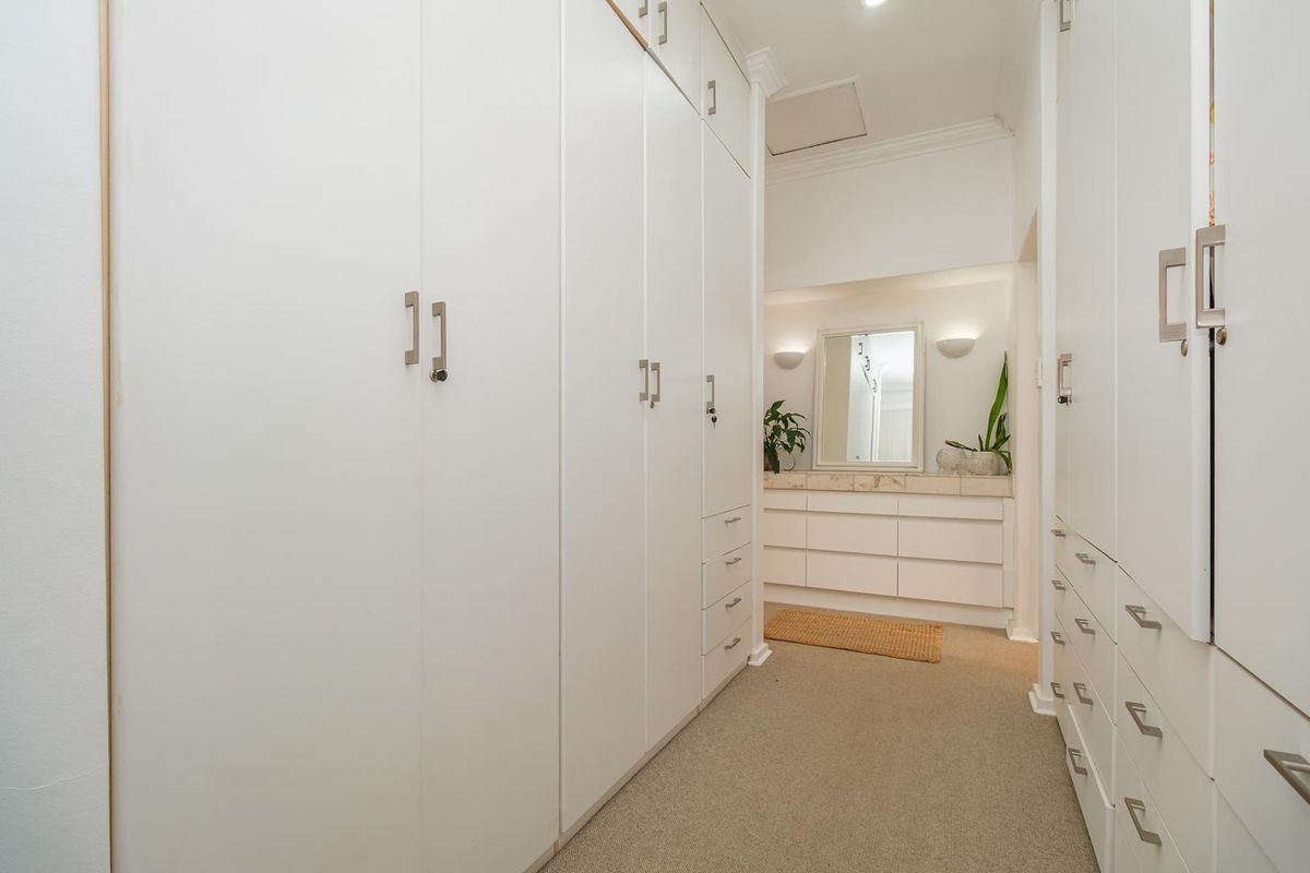 A spacious dressing area featuring extensive built-in white cabinetry, a vanity station with stone countertop, and elegant wall lighting.