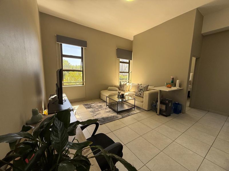 A bright living room featuring tiled flooring and large windows with roller blinds, offering a comfortable and functional living space.