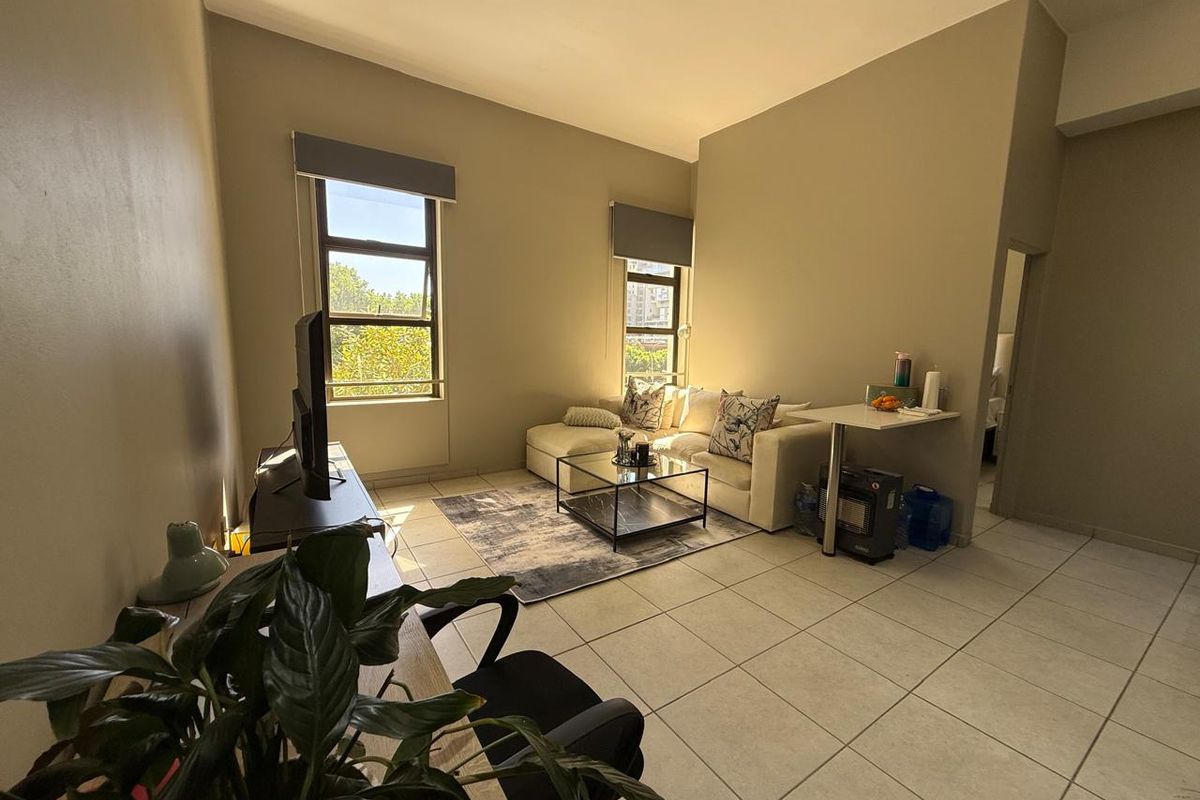 A bright living room featuring tiled flooring and large windows with roller blinds, offering a comfortable and functional living space.