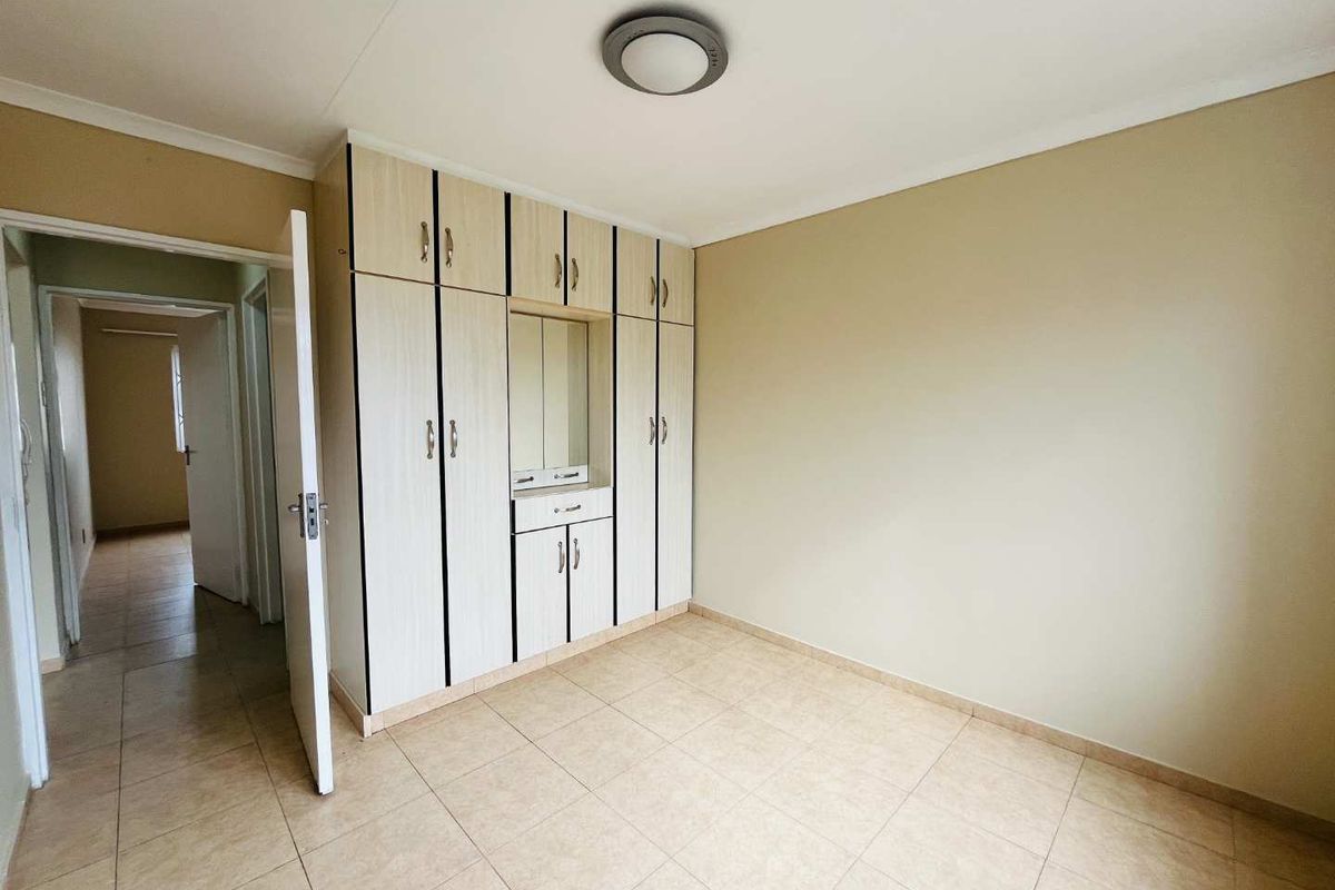 A clean, empty bedroom featuring neutral tiled flooring and floor-to-ceiling built-in cupboards with integrated vanity mirror.