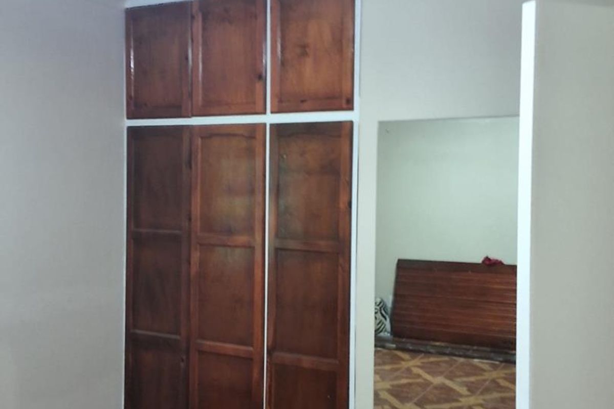 A bedroom featuring built-in wooden wardrobes, tiled flooring, and a wooden ceiling, offering a functional space with classic finishes.