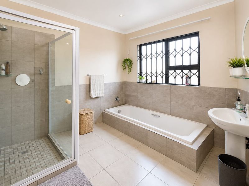 A well-maintained bathroom featuring a built-in bathtub, a separate glass-enclosed shower, and a pedestal basin with neutral tiled finishes.