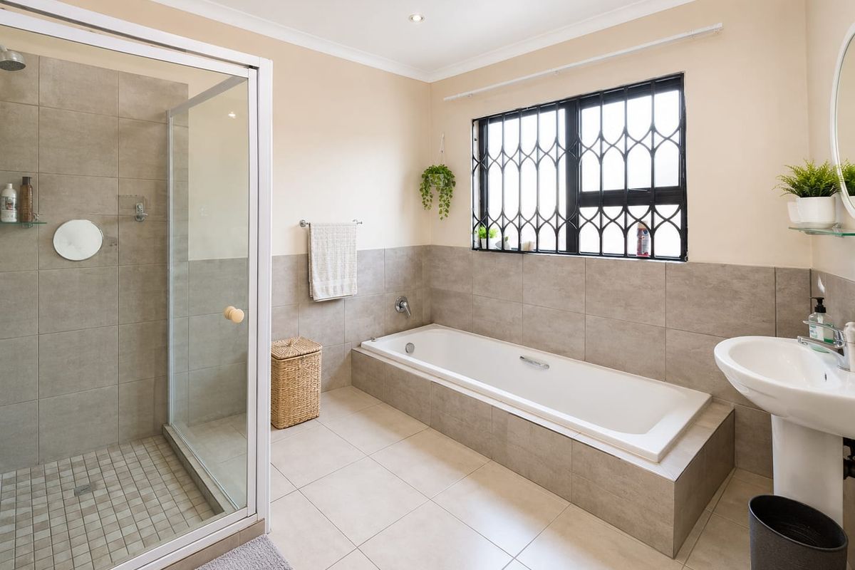 A well-maintained bathroom featuring a built-in bathtub, a separate glass-enclosed shower, and a pedestal basin with neutral tiled finishes.