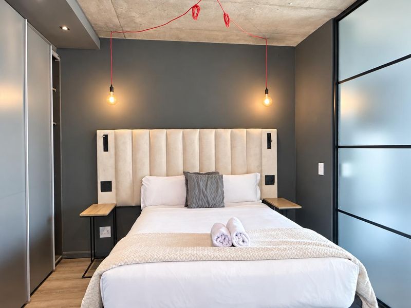 Modern bedroom featuring an exposed concrete ceiling, built-in wardrobe, and a stylish frosted glass partition wall.