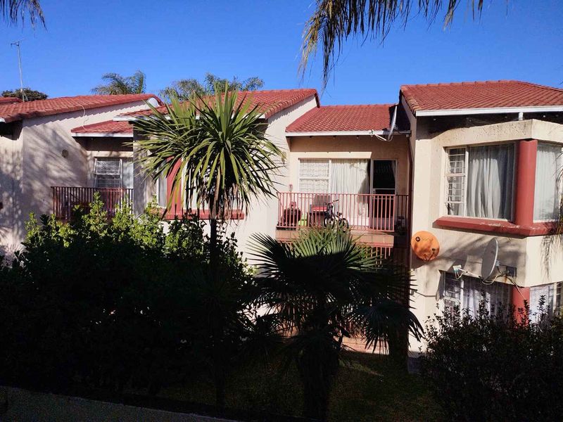 Rear view of a multi-story apartment complex featuring terracotta tiled roofing, private balconies with metal railings, and established garden landscaping.