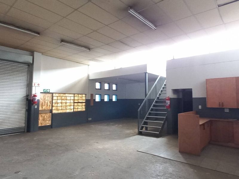 Spacious industrial open-plan unit featuring a large roller shutter door, mezzanine staircase, kitchenette area, and functional lighting, suitable for various commercial or storage uses.