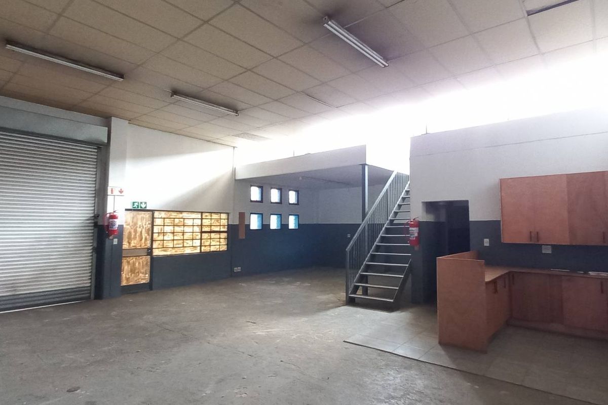 Spacious industrial open-plan unit featuring a large roller shutter door, mezzanine staircase, kitchenette area, and functional lighting, suitable for various commercial or storage uses.