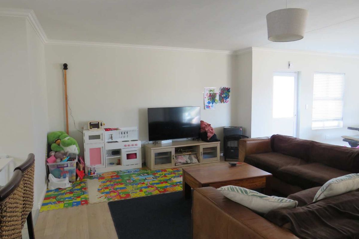 A spacious living room featuring neutral walls, laminate flooring, and natural light through venetian blinds, providing a comfortable and functional family living area.