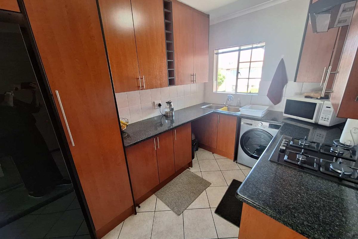 A functional kitchen featuring wood-veneer cabinetry, granite countertops, a built-in gas hob, and integrated space for a washing machine.
