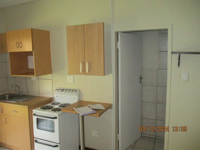 A compact kitchen featuring laminate cabinetry, a stainless steel sink, and a freestanding electric stove, with tiled splashbacks and flooring.