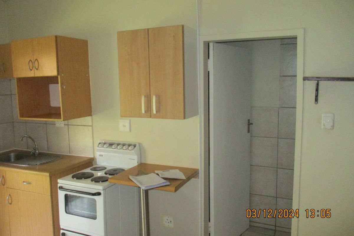 A compact kitchen featuring laminate cabinetry, a stainless steel sink, and a freestanding electric stove, with tiled splashbacks and flooring.