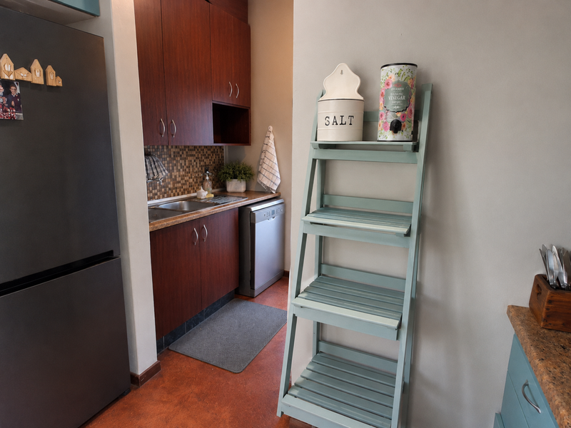 A functional scullery area featuring dark wood cabinetry, a mosaic tile backsplash, stainless steel sink, and integrated dishwasher.