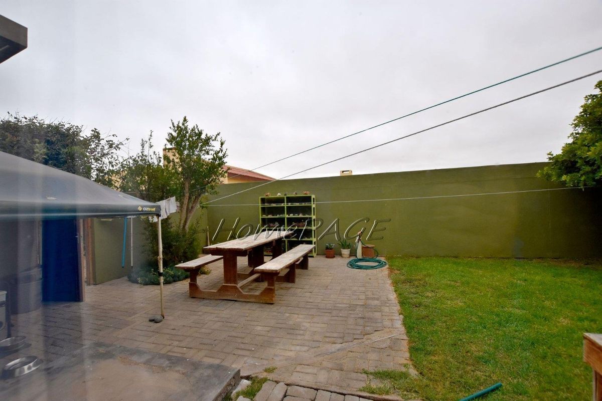 A rear garden area featuring paved patio space, a grass lawn, and a solid boundary wall, suitable for outdoor relaxation and entertainment.