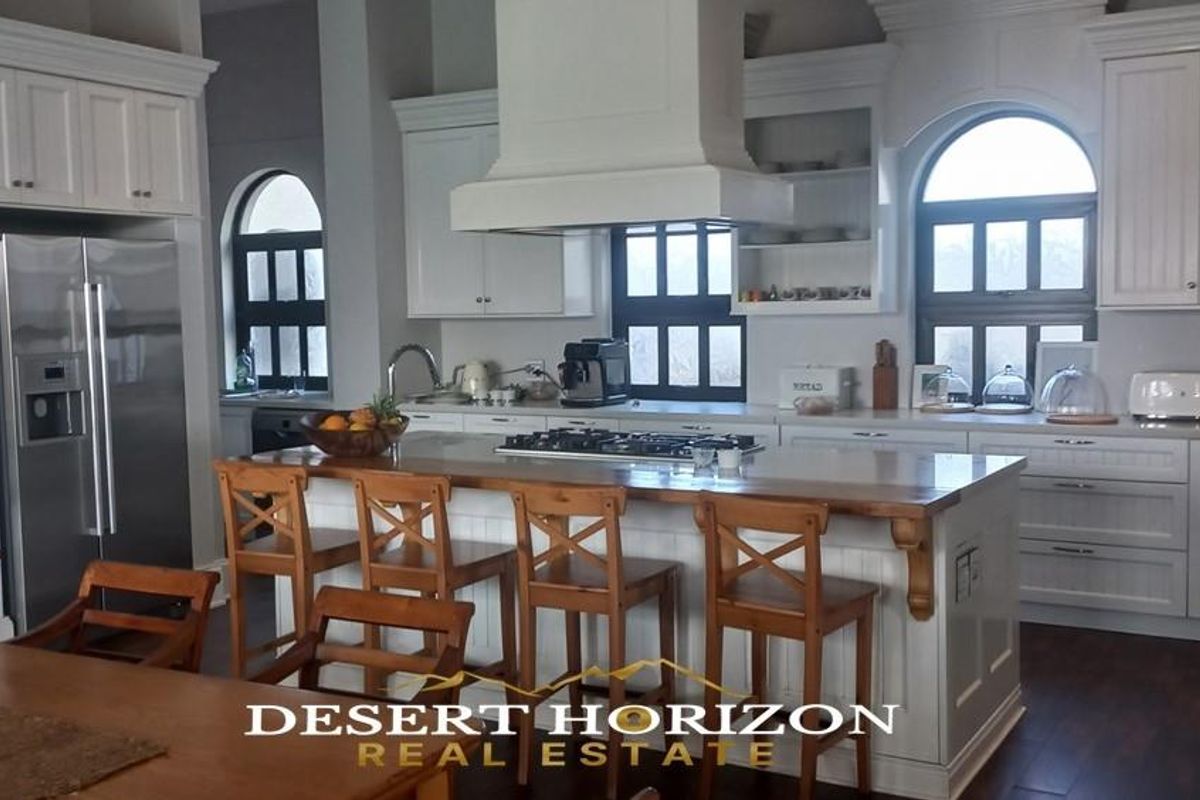 Spacious kitchen featuring white cabinetry, a central island with a gas hob, integrated appliances, and arched windows providing natural light.