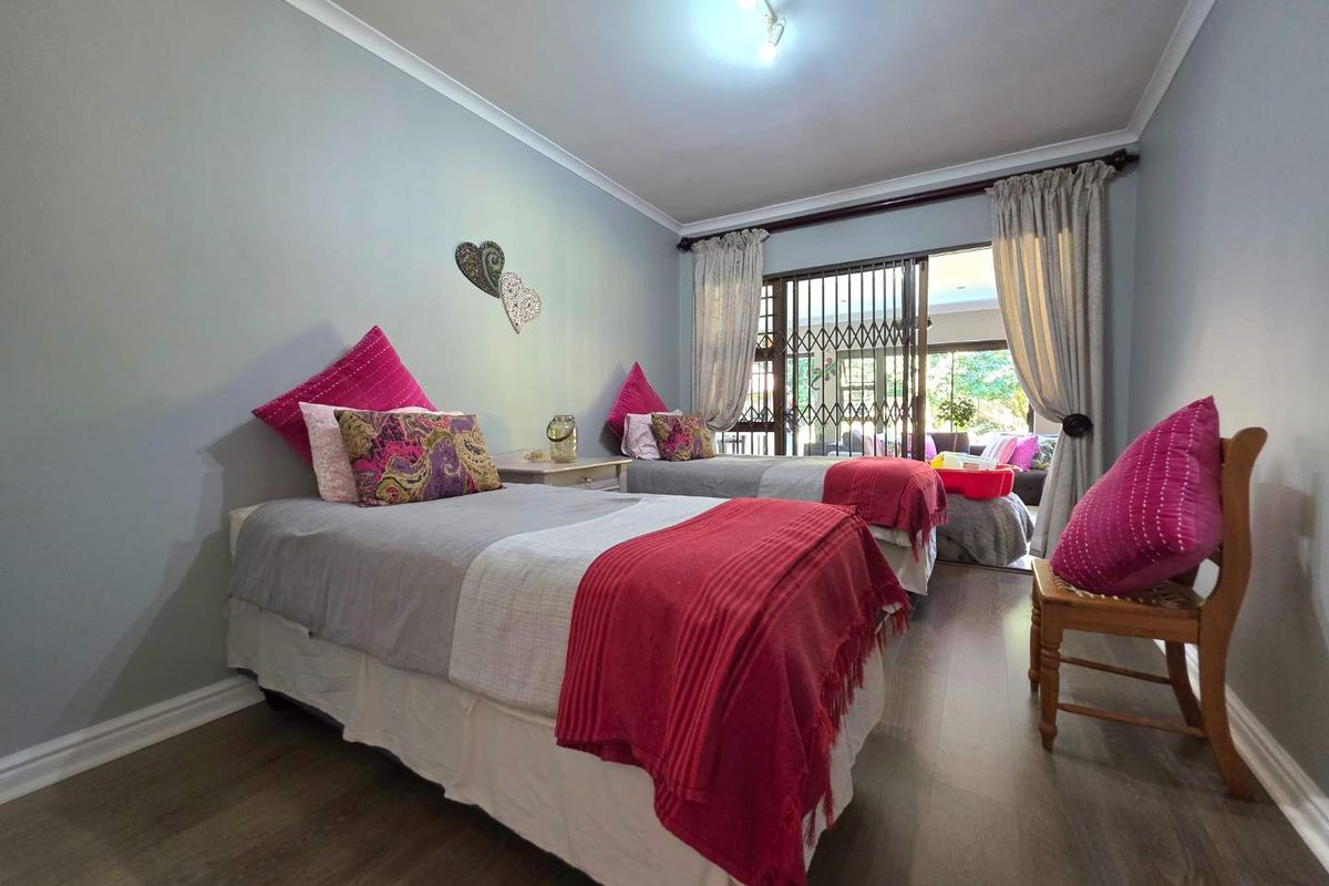 A well-lit bedroom featuring laminate flooring, coved ceilings, and a sliding glass door with security gate providing access to an outdoor area.