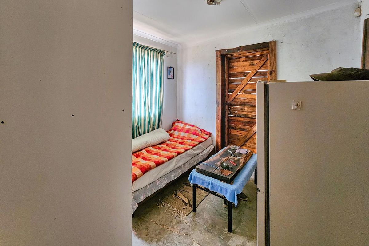 A small bedroom featuring exposed concrete flooring, a rustic timber door, and basic wall finishes, requiring cosmetic updates and repairs.