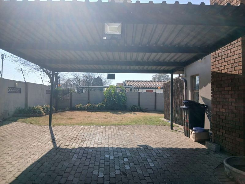 A covered carport area featuring a corrugated metal roof, paved flooring, and direct access to the rear garden and perimeter walling.