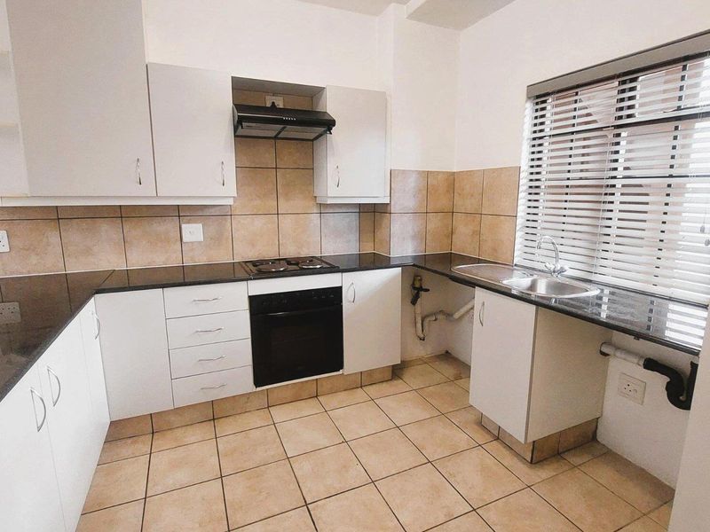 A functional kitchen featuring white cabinetry, dark granite countertops, built-in oven and hob, tiled splashbacks, and tiled flooring.