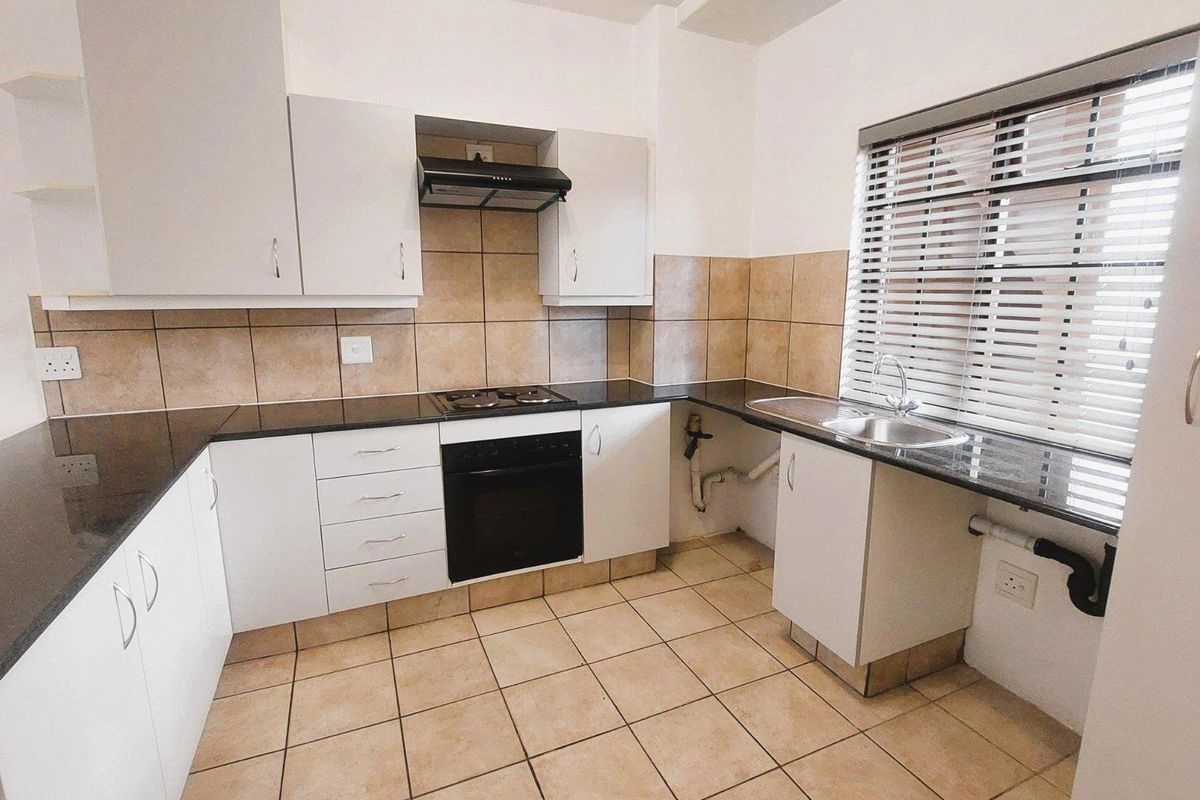 A functional kitchen featuring white cabinetry, dark granite countertops, built-in oven and hob, tiled splashbacks, and tiled flooring.