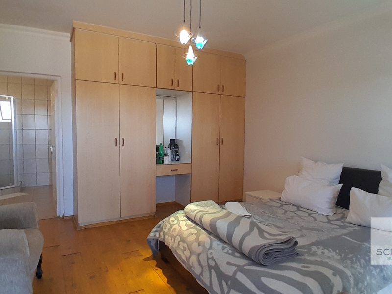 Spacious bedroom featuring light wood built-in cupboards, warm wooden flooring, and direct access to an en-suite bathroom.