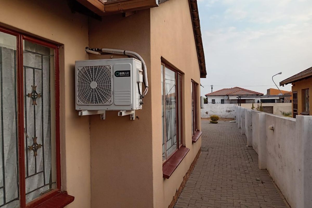 Side exterior view of the house featuring a paved walkway, security bars on windows, and a wall-mounted air conditioning unit.