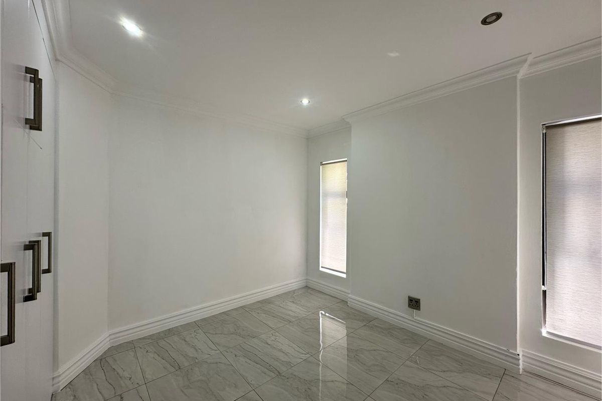 A bright, empty bedroom featuring polished marble-look floor tiles, recessed downlighting, crown molding, and built-in cabinetry.