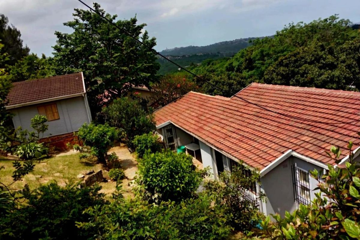 An elevated view of the property featuring tiled roofs, security bars on windows, and a surrounding garden area with mature trees.