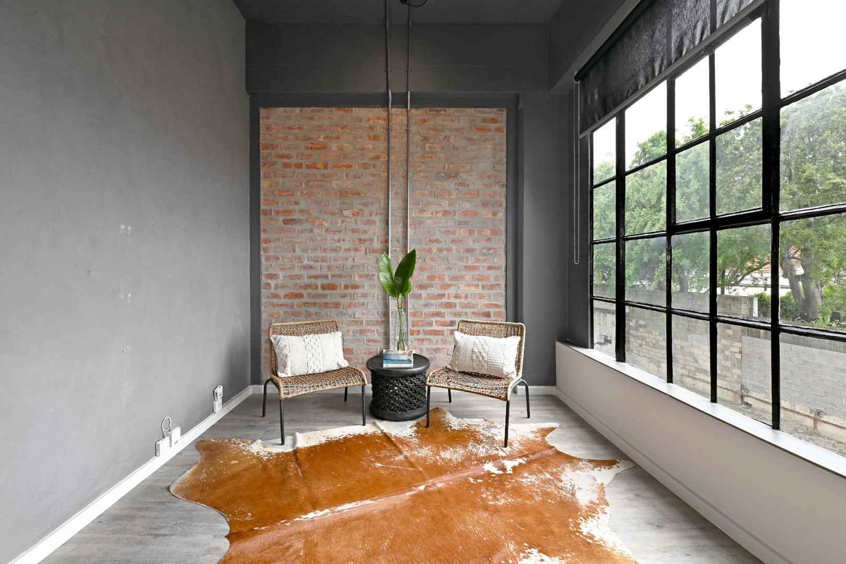 A bright living area featuring an exposed brick feature wall, industrial-style black metal windows, and modern laminate flooring.
