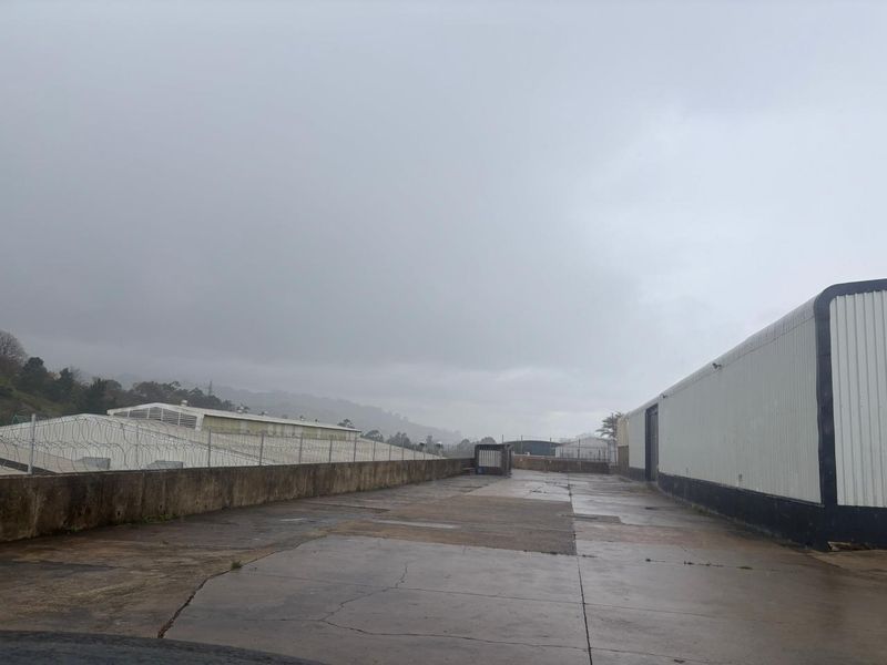 An industrial exterior yard area featuring concrete paving, metal-clad building walls, and perimeter security fencing with razor wire.