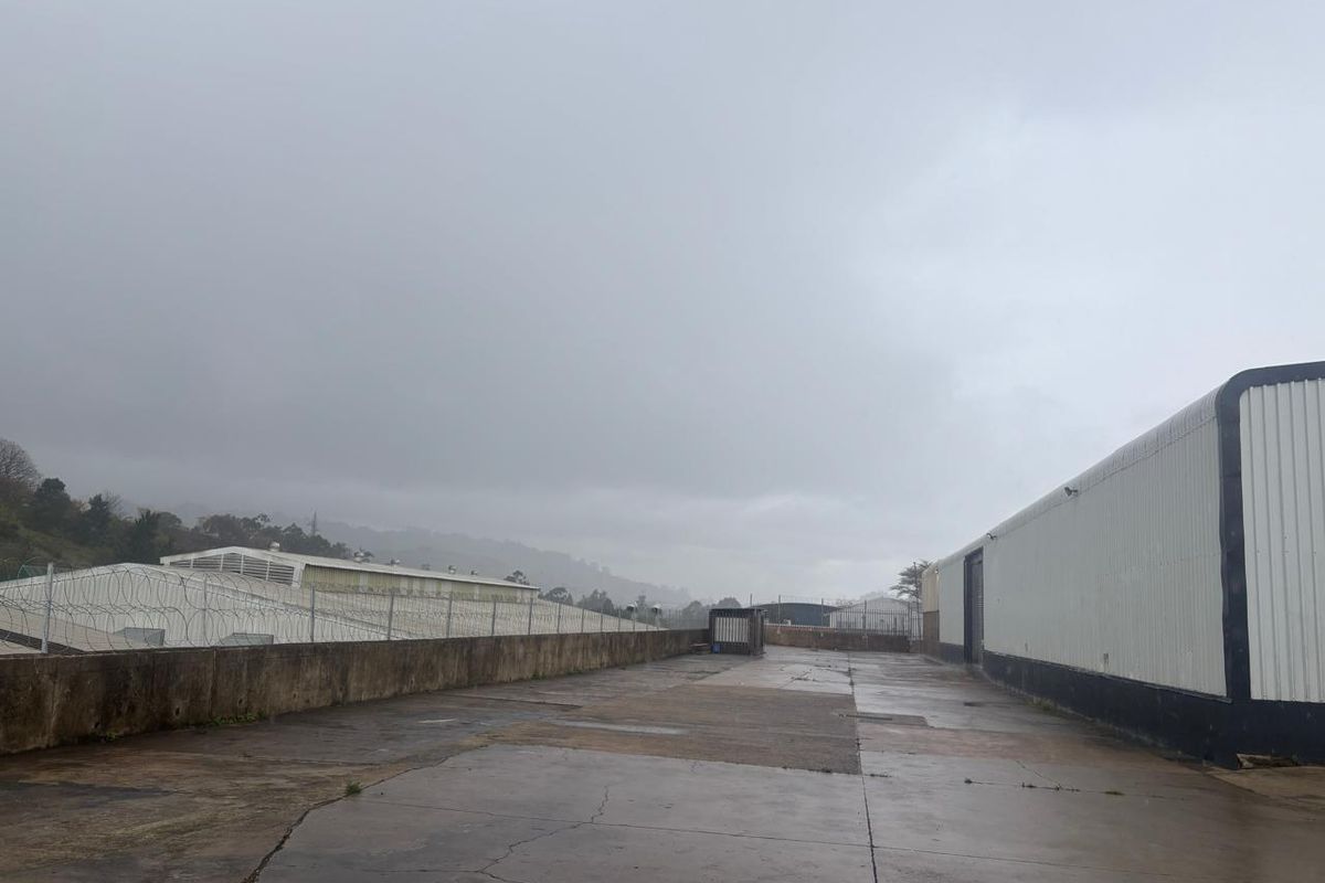 An industrial exterior yard area featuring concrete paving, metal-clad building walls, and perimeter security fencing with razor wire.