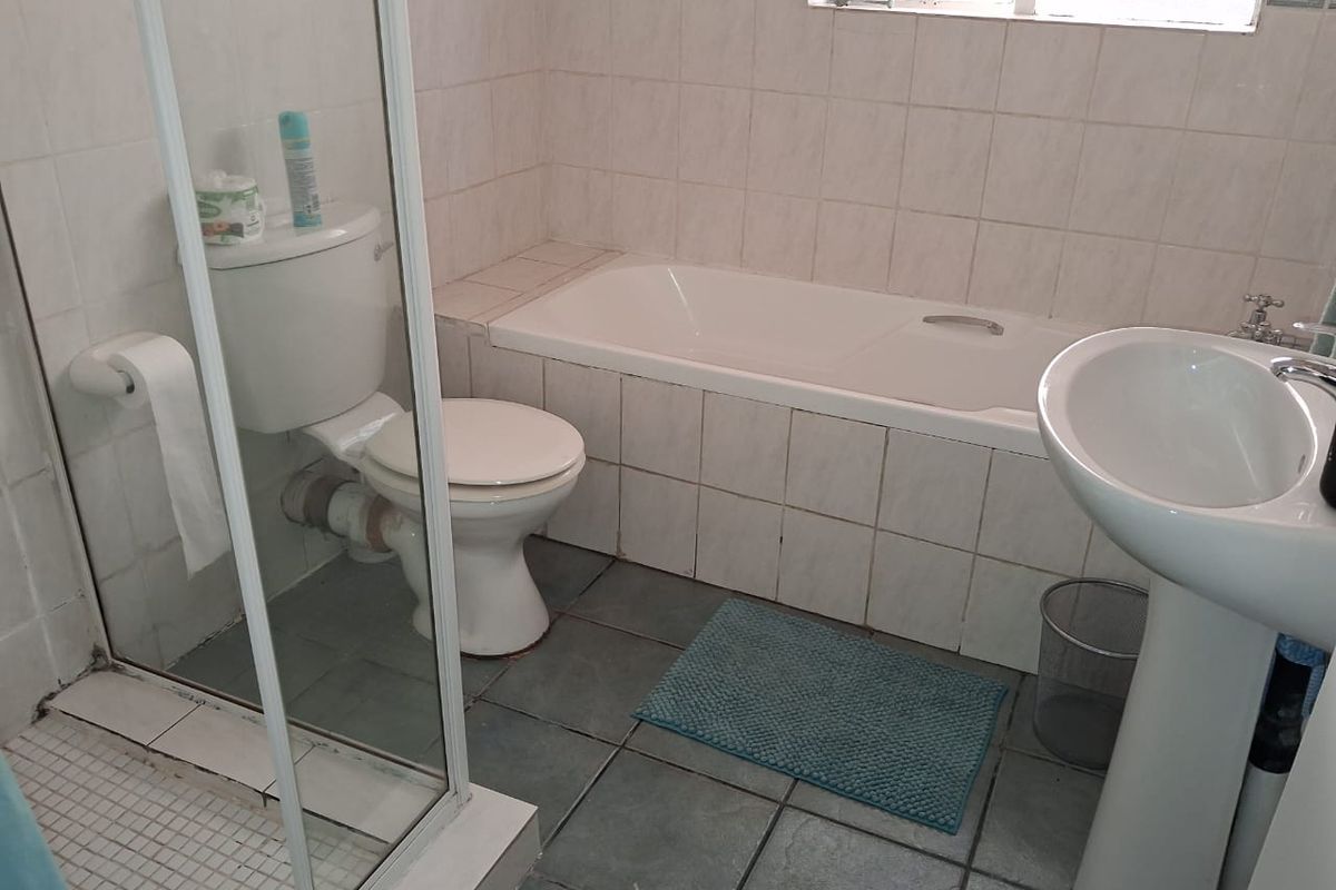 A functional bathroom featuring a shower enclosure, bathtub, pedestal basin, and toilet with tiled finishes throughout.