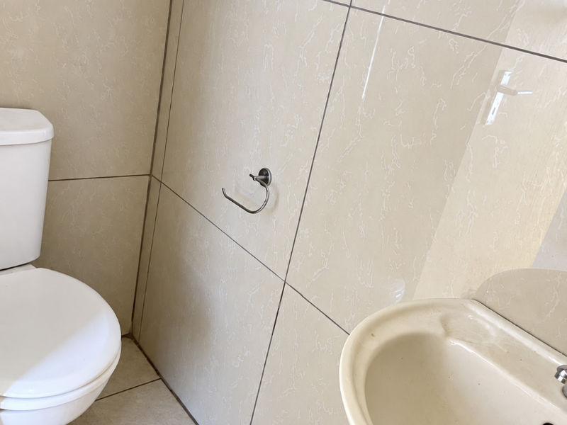 A compact bathroom featuring ceramic wall and floor tiling, a pedestal basin, and a standard toilet.