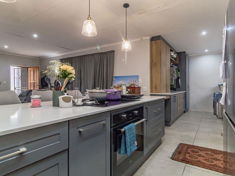 Modern open-plan kitchen featuring a central island with built-in oven and cooktop, complemented by sleek cabinetry and contemporary pendant lighting.