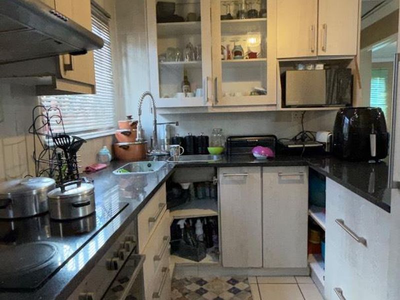 A functional kitchen featuring built-in cabinetry, glass-fronted display units, integrated oven, electric cooktop, and a stainless steel sink with a modern faucet.