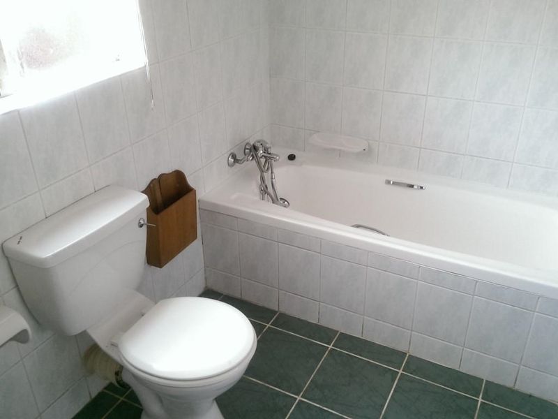 A functional bathroom featuring white wall tiles, green floor tiles, a standard bathtub, and a toilet.