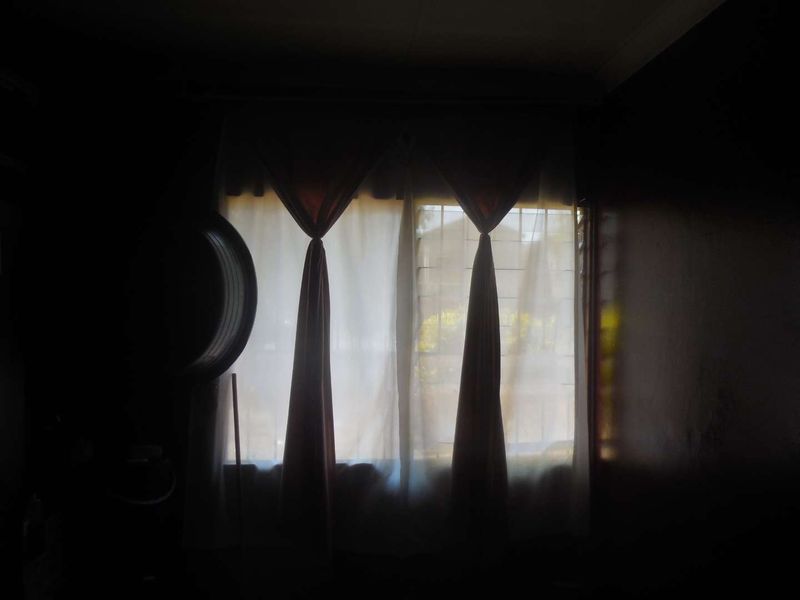 A dimly lit room featuring a window with security bars and curtain fixtures, currently obscured by low light conditions.