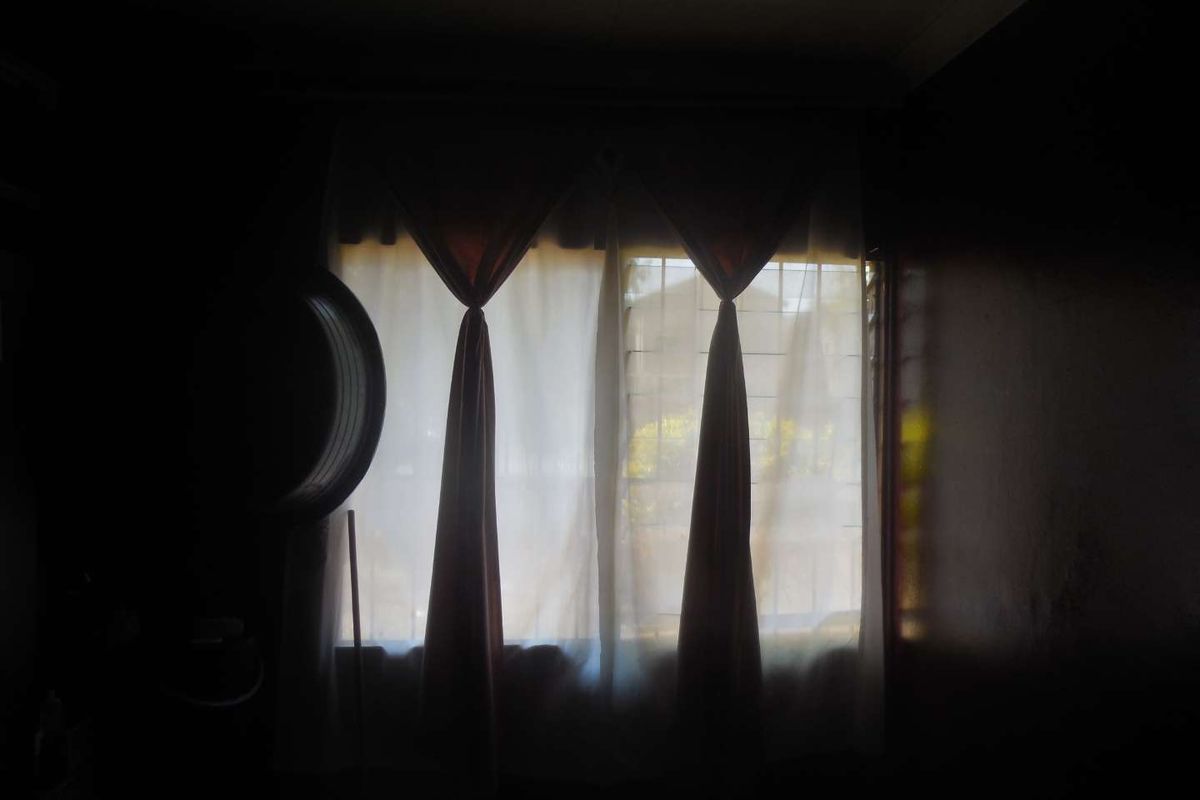A dimly lit room featuring a window with security bars and curtain fixtures, currently obscured by low light conditions.