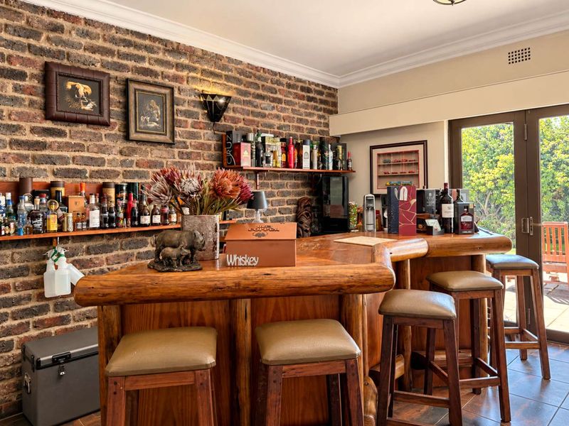 A rustic home bar area featuring an exposed brick wall, custom timber bar counter, and direct access to the outdoor patio through glass doors.